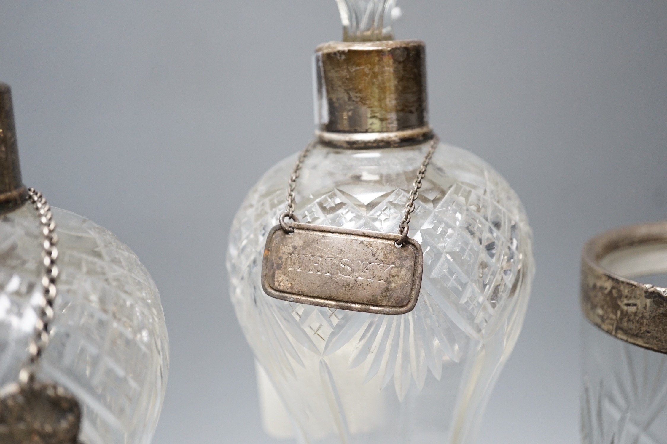 A collection of silver mounted glass items, including a pair of waisted decanters with two silver wine labels, a pair of vases, powder jar etc. and an Indian white metal jar and cover.